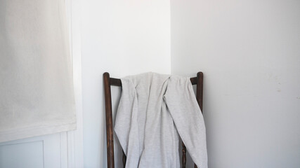 Sudadera gris en silla de madera en habitación de paredes blancas