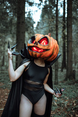 mask in the form of a pumpkin with burning eyes. creepy Halloween girl costume with long claws. cosplay of a demon in a mask. sexy outfit black bodysuit and long cape