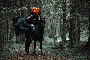 the rider is sitting astride a horse. a girl in a long black raincoat with a pumpkin mask with burning eyes. Creepy cosplay shooting for Halloween in the autumn forest. a cloak fluttering in the wind