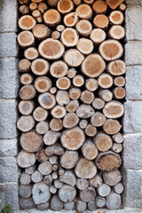 round firewood stacked neatly against the stone wall of the house