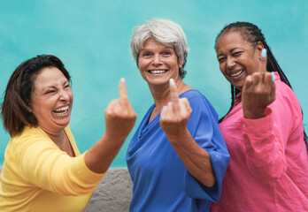 Multiracial senior women showing middle finger on camera - Crazy elderly friendship concept