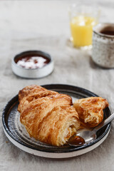 Breakfast with croissant, jam and hot chocolate, juice and tangerine on greige linen tablecloth. Selective focus