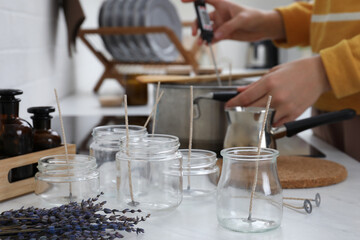 Woman making aromatic candles at white table indoors, focus on empty jars