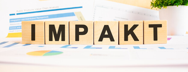 IMPAKT word on wooden cubes. The background is a business graphs. Business and finance concept