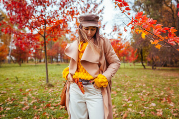 Stylish woman wears yellow sweater holding handbag in autumn park. Fall female clothes and accessories. Fashion