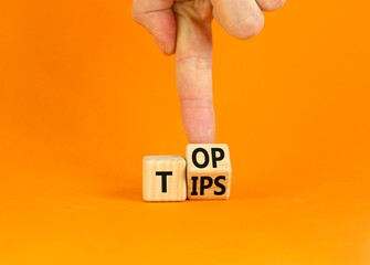 Top tips symbol. Businessman turns a wooden cube with words 'Top tips'. Beautiful orange table,...