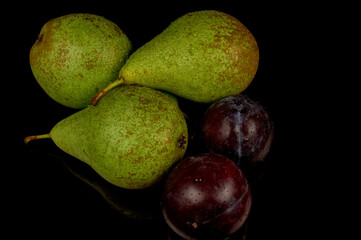 Fresh and wet pears and plums on a black background. Water drops on fruits