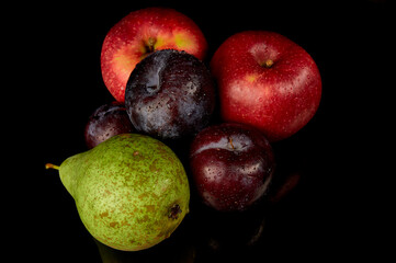 Red apple, green pear and plum on a black background. Water droplets on fresh fruit