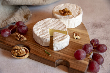 Cheese with white mold, grapes and walnuts on a wooden cutting board .