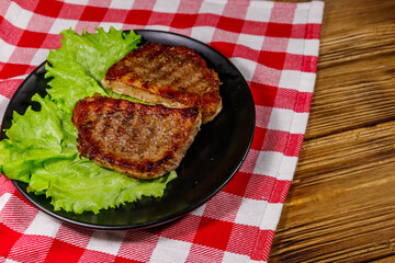 Grilled pork steaks with lettuce leaves on wooden table