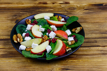Autumn spinach salad with apple, feta cheese, walnut and dried cranberry on wooden table. Healthy vegetarian food