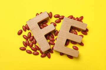 Wooden letters FE and pills on yellow background, flat lay. Anemia treatment