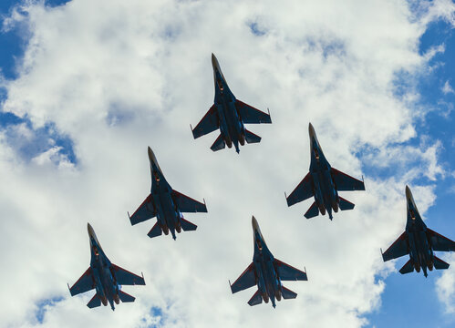 A squadron of jet soldiers, fighters, and airplanes perform a maneuver against the background of a blue and cloudy sky
