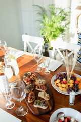 Table setting with snacks for a home party in Italian style. bruschetta with different fillings, seasonal fruits, homemade lemonade and wine glasses. Beautiful evening light from the window