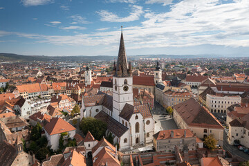 Fototapeta premium Landmarks of Romania. Aerial view of the old center of Sibiu city at the bottom of Fagaras Mountains during a beautiful sunny day with blue sky. Evangelical Cathedral after restoration.
