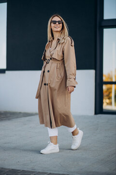 Young blonde woman in beige coat walking in the street