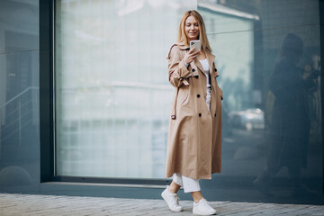 Young woman in beige trench using phone outside