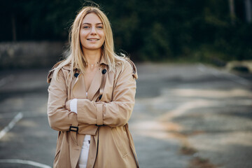 Young blonde woman in beige coat walking in the street