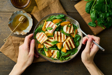 Eating delicious summer vegetarian healthy salad with orange tomatoes, fresh spinach, halloumi...