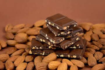 Milk chocolate cubes on heap with almonds stock images. Pieces of almond chocolate on a brown background stock images