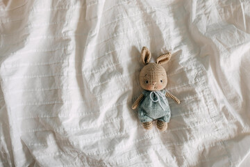 Crocheted bunny toy in a green romper on white bed sheet.