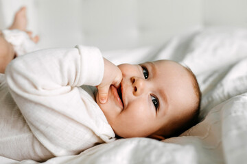 Fototapeta na wymiar Baby lying in bed, smiling, sucking fingers.
