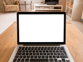 Laptop mockup on a wooden table in a living room. White screen in a home office with point of view of a worker. Computer display and keyboard in a small cozy room. Notebook monitor for modern business