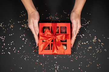 Various handmade chocolate truffle candies in a red box on a dark background in female hands.