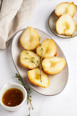 Caramelized pear halves on an oval grey plate with thyme branches and caramel on a white table surface, top view