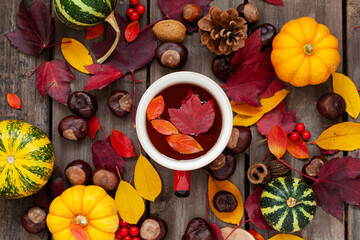 Autumn flat lay. Red mug with hot herbal tea. Pumpkins, bright maple leaves, wooden background. Top view close up