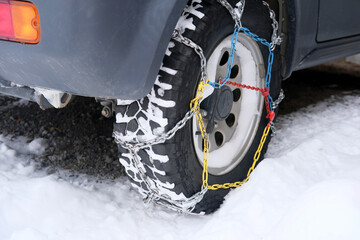 close-up wheel of a gray car in colored iron chains on the snow, winter travel safety concept with...