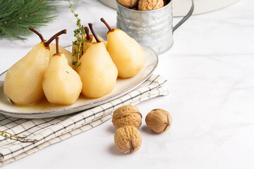 Peeled poached pears on a white oval plate on a checkered linen cloth and a christmas fair-tree branch on a white table surface