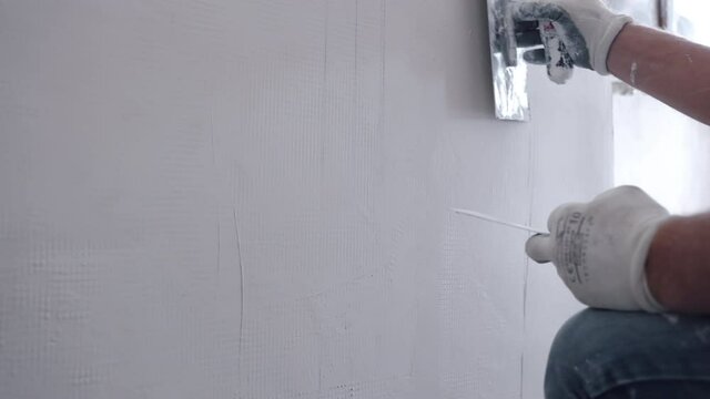 Workman reconstructing old ruined wall on construction site, builder levelling concrete wall with metal spatula putting white paste stucco and wiping. Repairman plastering walls at home, aligning wall