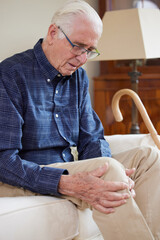 Senior Man Sitting On Sofa At Home Suffering With Knee Pain From Arthritis