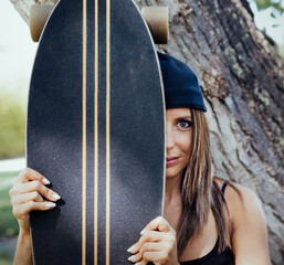general shot of light-eyed Caucasian girl, hiding behind a skateboard. she has a cap and long hair....