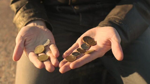 A poor man in worn down clothes counting coins in palms of his hands. A beggar counts the change he could earn begging for money. A broken person got into poverty, been laid off. Unemployment