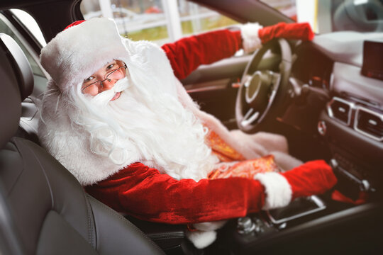 Santa is smiling with his hands on the steering wheel of a new car.