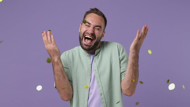 Smiling cheerful happy attractive charming stunning young bearded man 20s years old wear mint shirt hold in hand throw away golden confetti isolated on plain light purple background studio portrait
