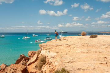 A young tourist looks at the horizon over the Mediterranean Sea from the edge of the rocky coastline, in the island of Formentera in Spain