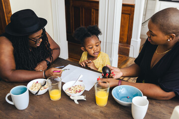 Lesbian parents teaching daughter while having breakfast at home