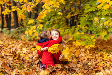 Happy children little girls cuddle in yellow maple leaves in autumn park outdoor