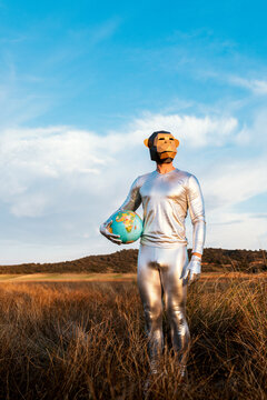 Male with geometric monkey mask holding globe in nature