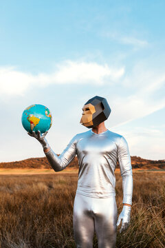 Male with geometric monkey mask holding globe in nature