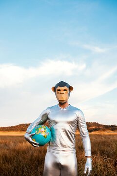 Male with geometric monkey mask holding globe in nature