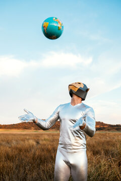 Guy in monkey mask tossing Earth painted ball in field