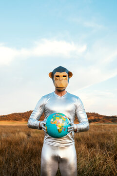 Male with geometric monkey mask holding globe in nature