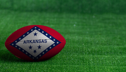 American football ball  with Arkansas flag on green grass background, close up