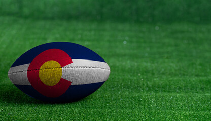 Fototapeta na wymiar American football ball with Colorado flag on green grass background, close up