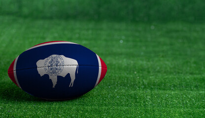 American football ball  with Wyoming flag on green grass background, close up