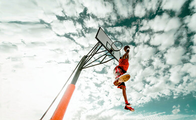Street basketball player making a powerful slam dunk on the court - Athletic male training outdoor on a cloudy sky background - Sport and competition concept	
